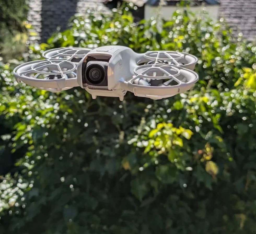 DJI Neo hovering outdoors against green foliage