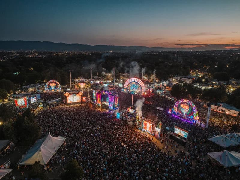Twilight aerial photography capturing vibrant music festival with illuminated stages and thousands of attendees
