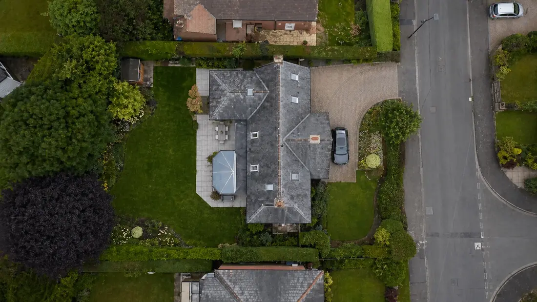 Top-down aerial photograph of a detached house showing the full roof, driveway, garden and surrounding street