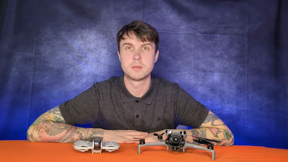 Peter Leslie behind a caged DJI Flip and an open-propeller DJI Mini 5 Pro on a table, showing the size difference between a caged indoor drone and a folding outdoor one