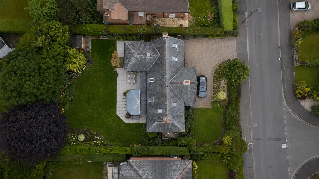 True top-down drone photograph of a detached house, showing the whole roof, the driveway, the garden layout and the street, with no horizon in the frame