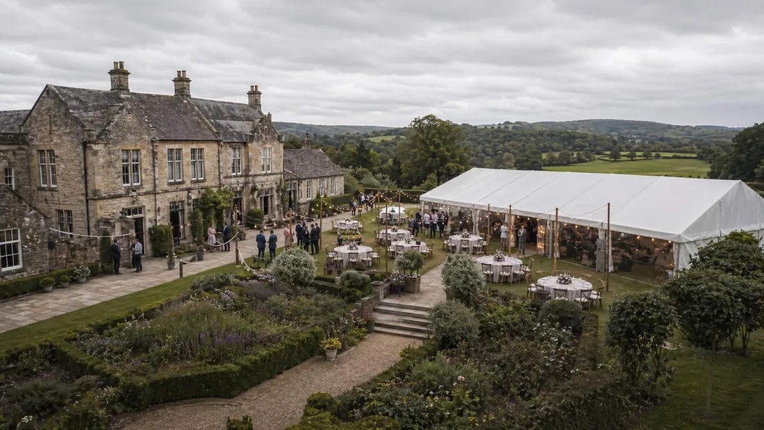 Elevated aerial photograph of a stone manor house with a marquee, formal garden and guests, taken from perhaps thirty metres up with rolling countryside behind