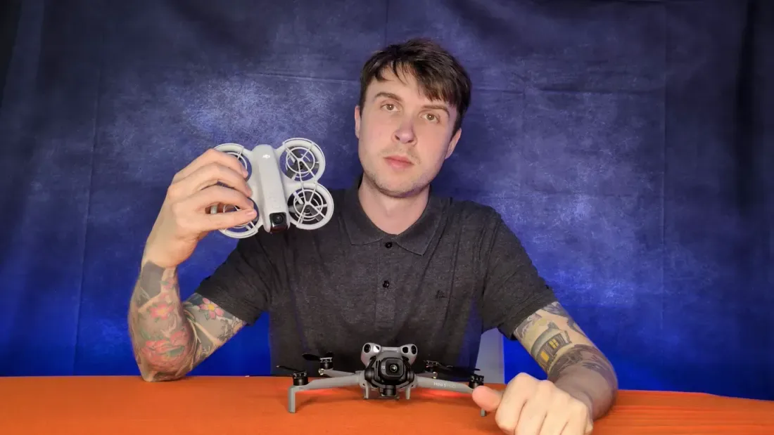 Peter Leslie holding a palm-sized DJI Neo up to the camera, with a folded DJI Mini 5 Pro on the desk in front of him