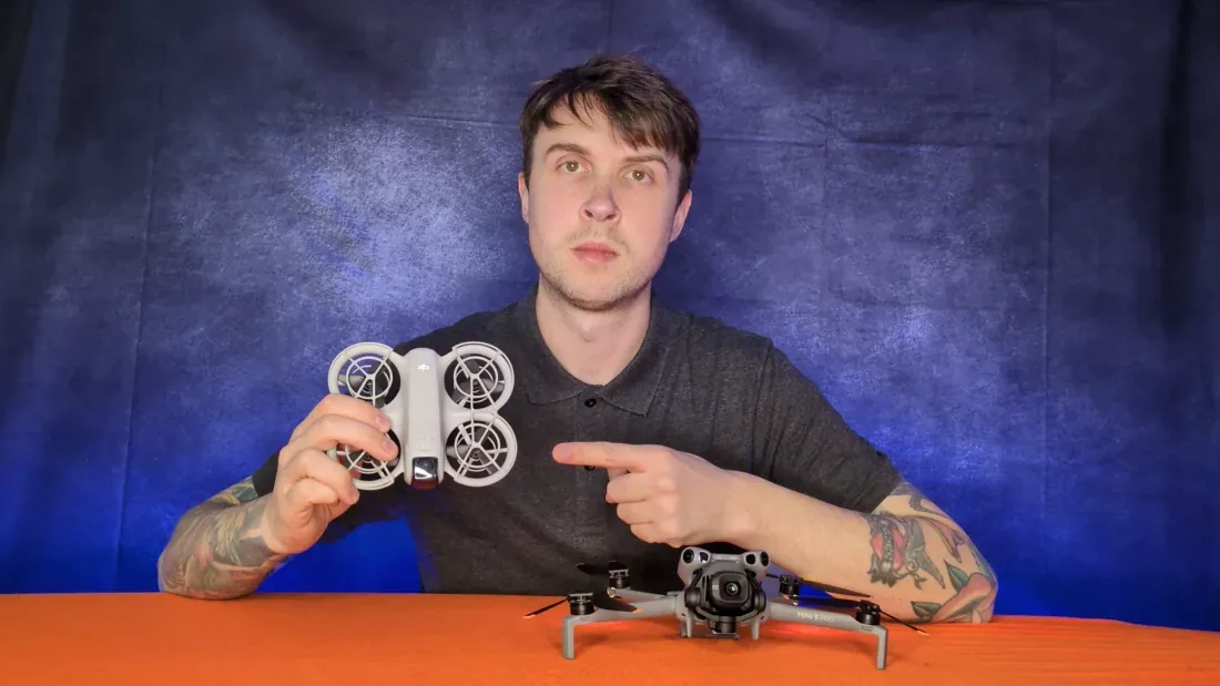 Peter Leslie holding a palm-sized DJI Neo up to the camera and pointing at it, with a DJI Mini 5 Pro on the desk in front of him