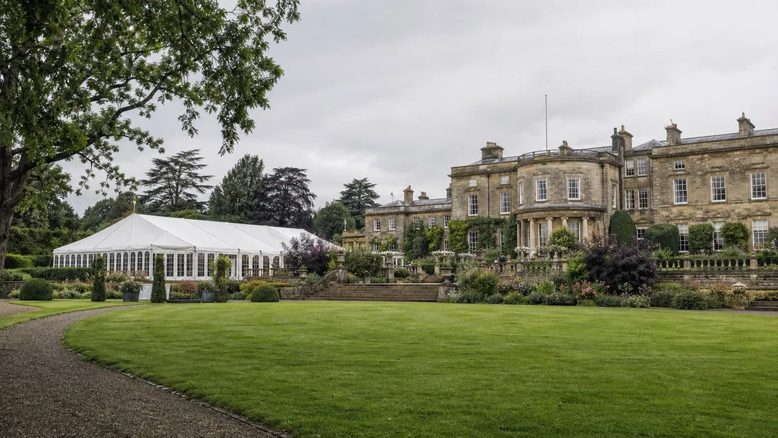 A country house with a marquee pitched on the lawn beside it, set up for a wedding with no guests yet arrived