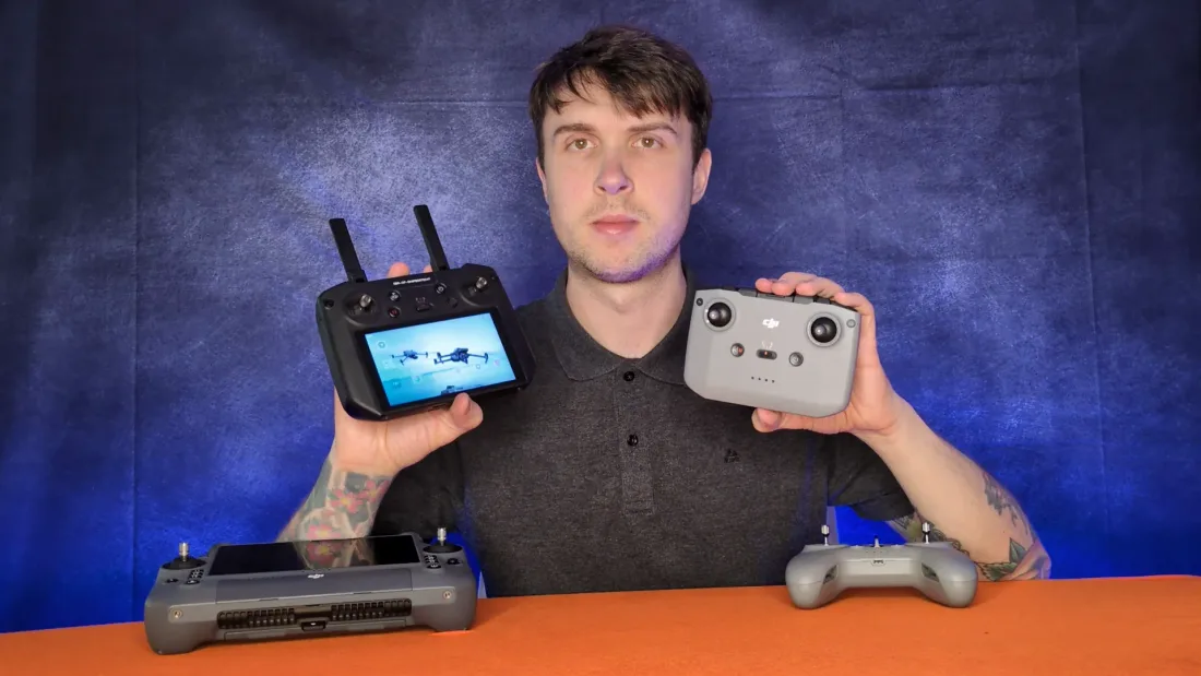 Peter Leslie holding up two DJI controllers, a screen-equipped smart controller and a plain RC-N3, with two more controllers on the desk in front of him