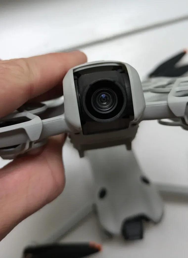 Close-up of a small DJI drone's three-axis gimbal and camera lens held between finger and thumb