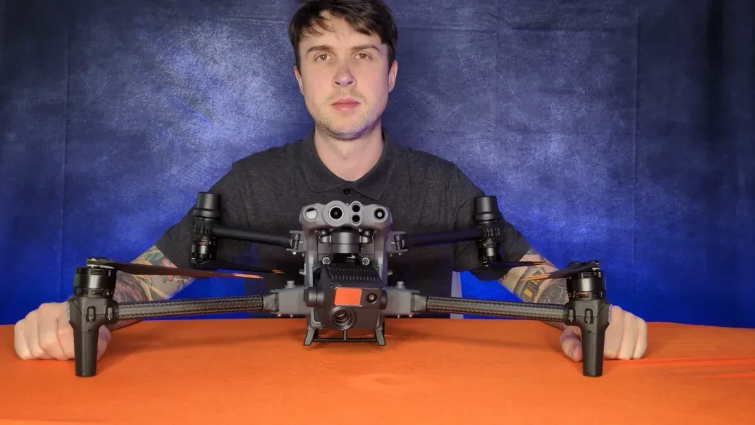 Peter Leslie holding a DJI Matrice enterprise drone by two of its four arms, showing the size difference against a folding consumer drone