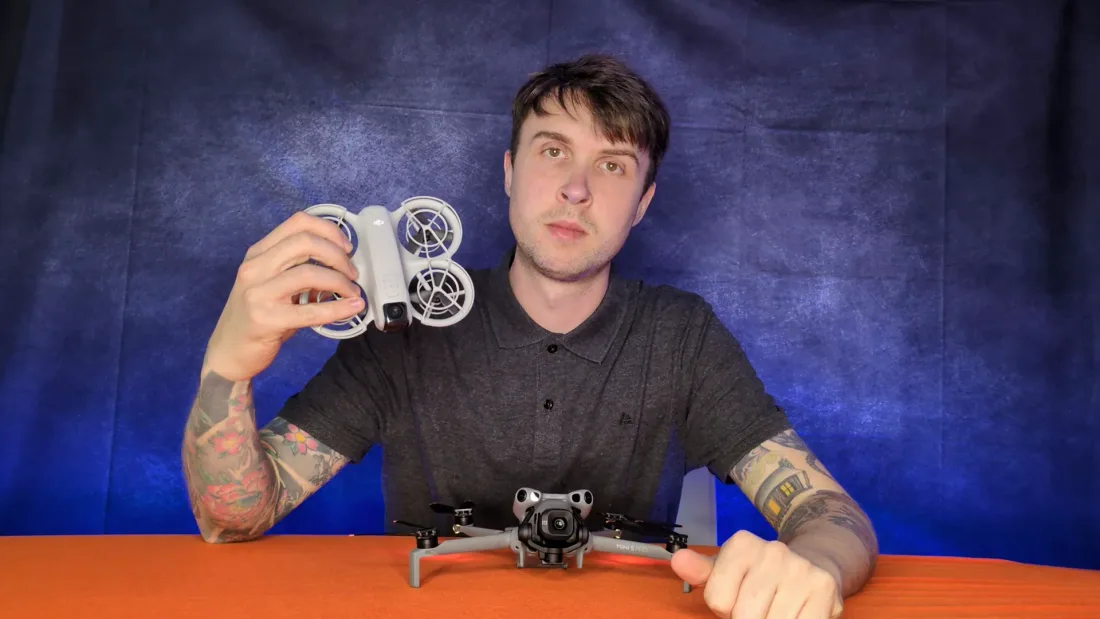 Peter Leslie holding up a DJI Neo 2 with its ducted propeller guards clearly visible, a DJI Mini 5 Pro on the table in front of him